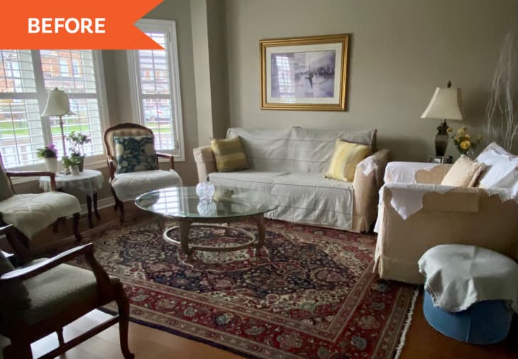 Traditional living room with white sofas, glass coffee table, patterned rug, and framed artwork.