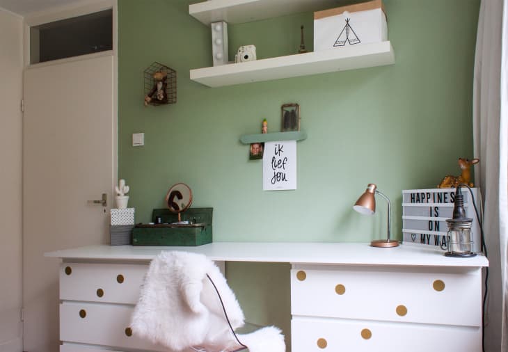 White desk with gold polka dots, green wall, shelves, lamp, and decor items including a lightbox and small deer figurine.