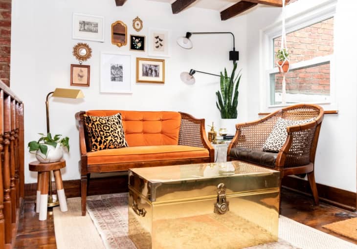 Cozy living room with orange sofa, cane chairs, gold trunk table, and gallery wall of framed art.