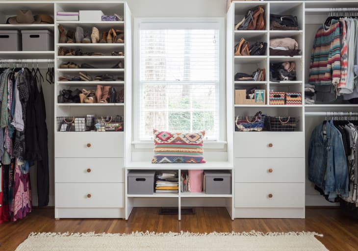 Organized walk-in closet with shelves of shoes, bags, and clothes, featuring a window seat with a colorful pillow.