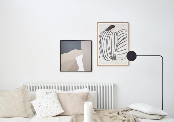 Minimalist bedroom with abstract art, beige pillows, and a black floor lamp.