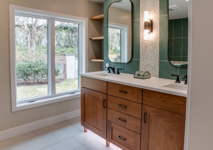 Bathroom with wood vanity and green tile behind mirrors.