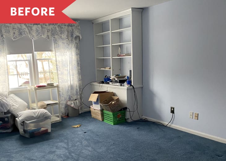 Cluttered room with blue carpet, built-in shelves, boxes, and a window with floral curtains.