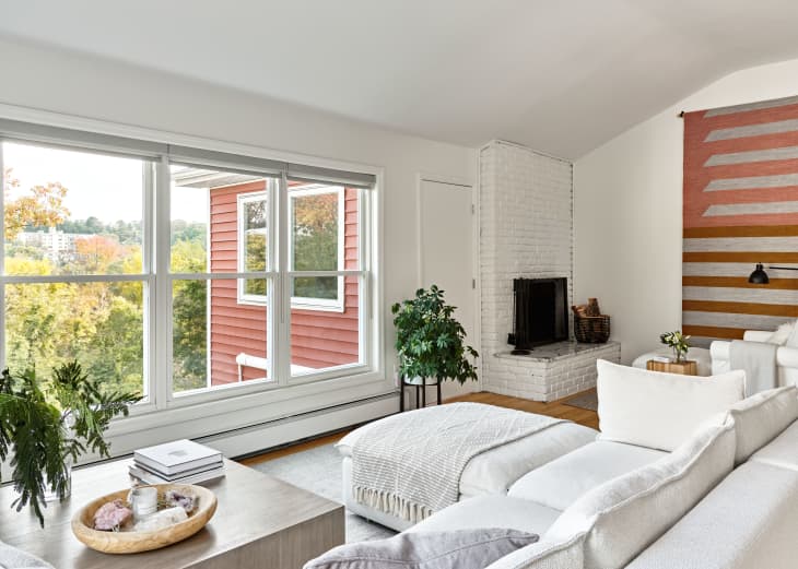 Bright living room with large window, white sectional sofa, potted plant, and brick fireplace.