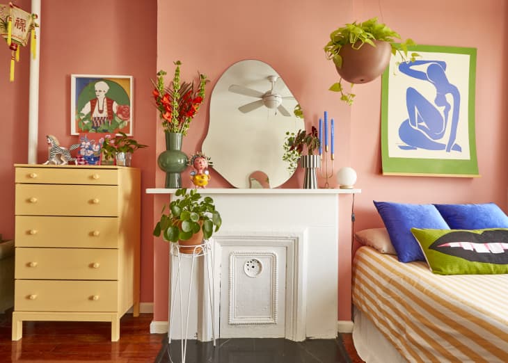 An organic-shaped mirror sitting on top of a white fireplace mantel along with candlesticks and flower vases in a peach bedroom