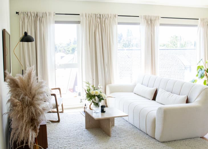An apartment living room with white walls, cream curtains, a white couch, and a white rug