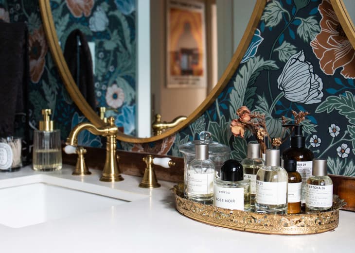 Floral print wall paper in bathroom with perfume collection in tray on bathroom vanity surface.