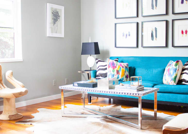 Living room with a teal sofa, colorful pillows, patterned coffee table, and framed art on the wall.