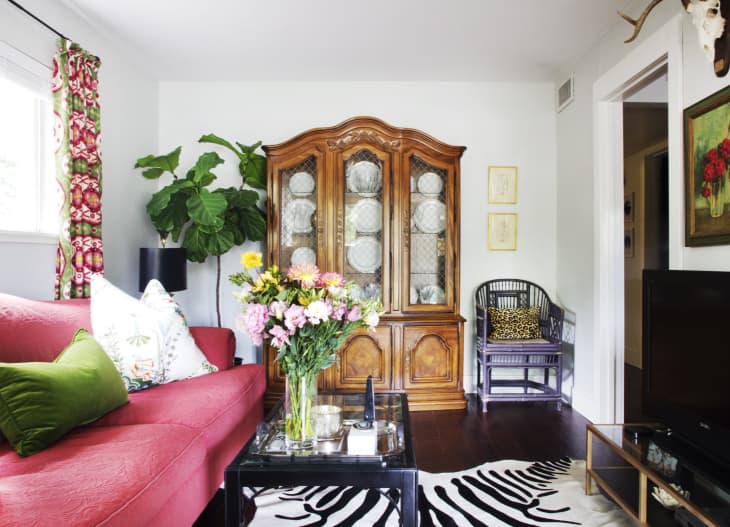 Living room with red sofa, green pillows, floral curtains, wooden cabinet, zebra rug, and a bouquet of flowers on a glass table.
