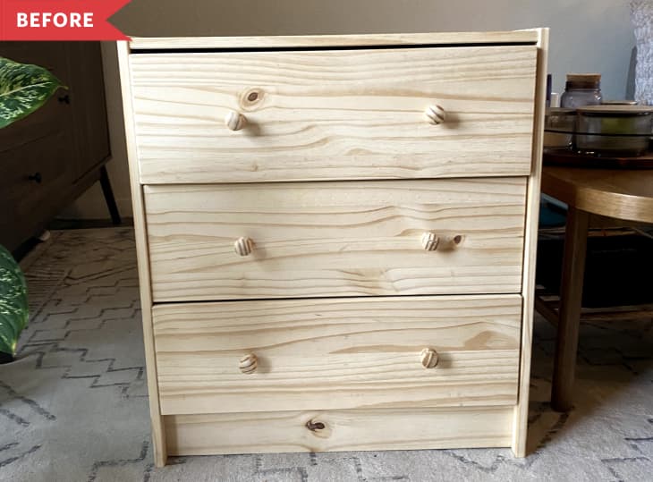 Unfinished wooden dresser with three drawers and round knobs, placed on a patterned rug next to a wooden table.