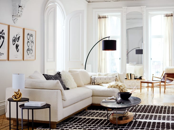 Living room with a cream sectional sofa, black floor lamp, round coffee table, and abstract wall art.