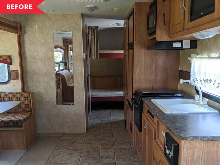 RV interior with wood cabinets, kitchenette, booth seating, and a view into the sleeping area with bunk beds.