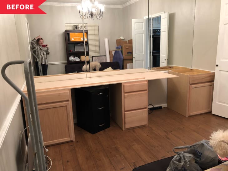 Home office with wooden cabinets, mirrored wall, chandelier, and cluttered shelves. Person taking a photo in the mirror.