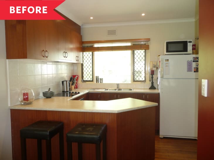 Small kitchen with wooden cabinets, white countertops, bar stools, and a white fridge.
