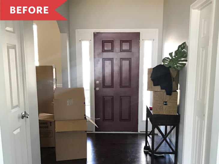 Entryway with maroon door, moving boxes, and a small table with a plant and black cloth.