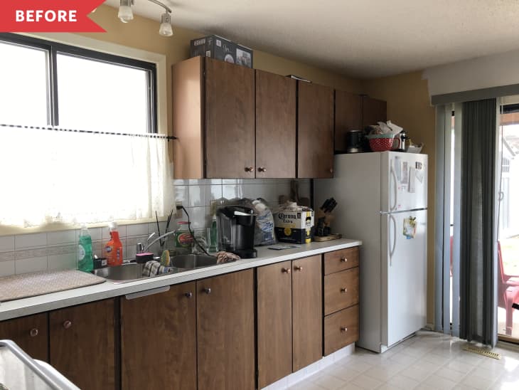 Cluttered kitchen with brown cabinets, white fridge, and various items on the counter, including a coffee maker and cleaning supplies.