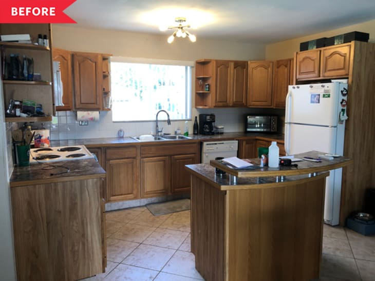 Wooden kitchen cabinets, white appliances, and a small island with cluttered countertops in a tiled kitchen.