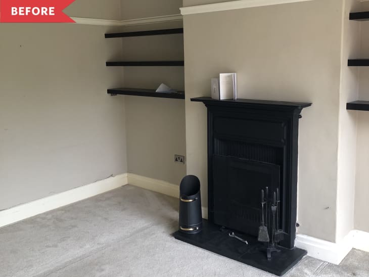 Empty living room corner with black fireplace, beige walls, black shelves, and a gray carpet.