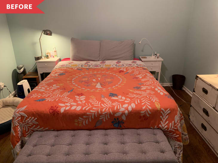 Bedroom with orange floral bedspread, gray tufted bench, white nightstands, and light blue walls.
