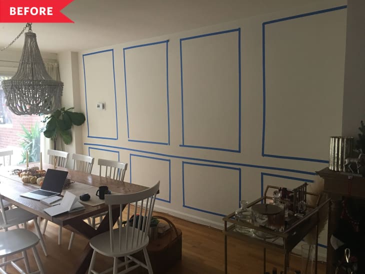Dining room with a wooden table, white chairs, laptop, and a large chandelier. Blue tape outlines on the wall.