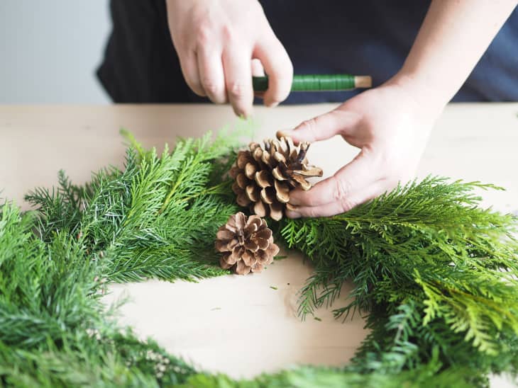 Woman adding pinecones to an evergreen wreath