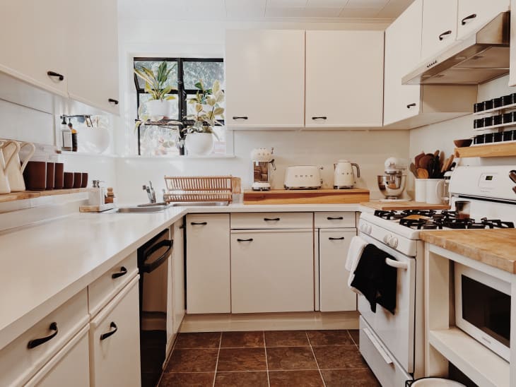Cozy kitchen with white cabinets, wooden countertops, potted plants, and various kitchen appliances.