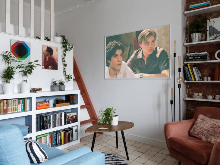 living room with blue loveseat, white walls, lots of plants, built-in shelves, art/photography on walls, wood art details