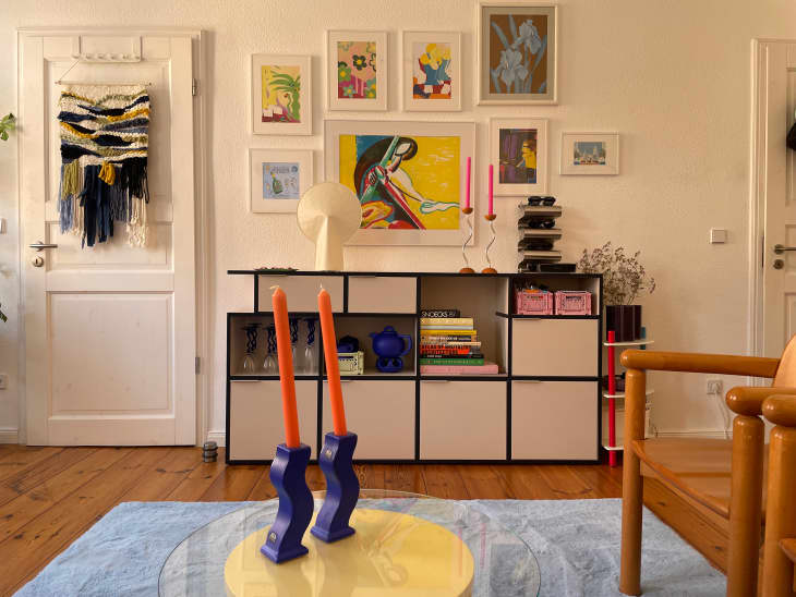 Colorful art filled gallery wall above shelving unit in living room.