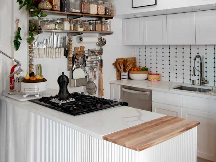Modern kitchen with a gas stove, white cabinetry, open shelving with jars, and a wooden countertop.
