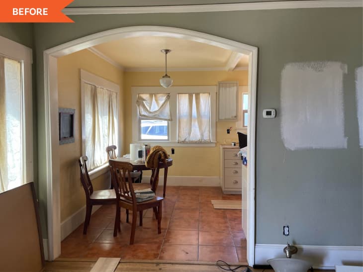 Dining area with wooden chairs, table, and yellow walls, adjacent to a kitchen with white cabinets and tiled floor.