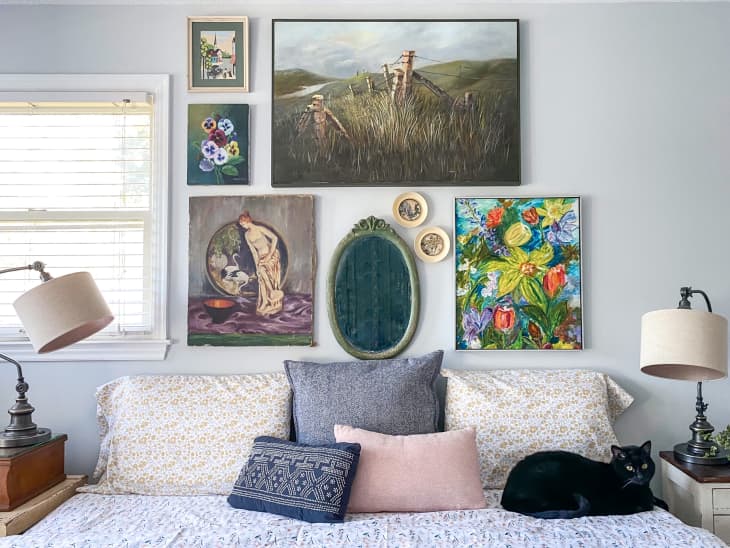 Gallery wall of paintings above bed with pillows and cat