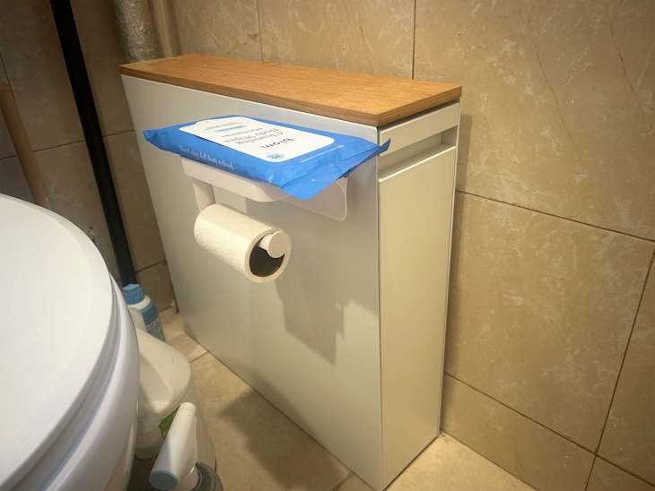 Bathroom corner featuring a white toilet, a modern white cabinet with a wooden top, and a toilet paper holder.