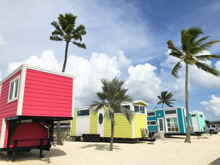 Colorful tiny houses on trailers with palm trees and a cloudy sky.