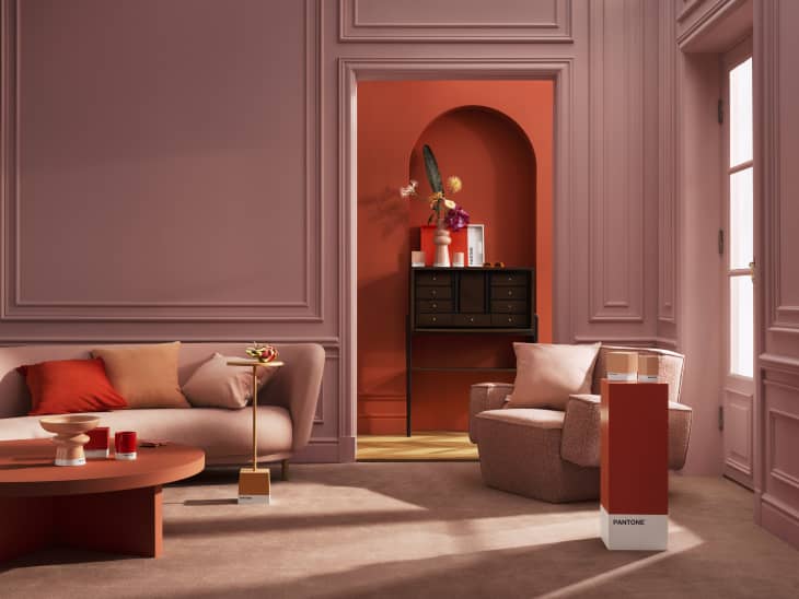 Living room with pink walls, beige sofa, red accents, and a black console table with decorative items in an arched alcove.