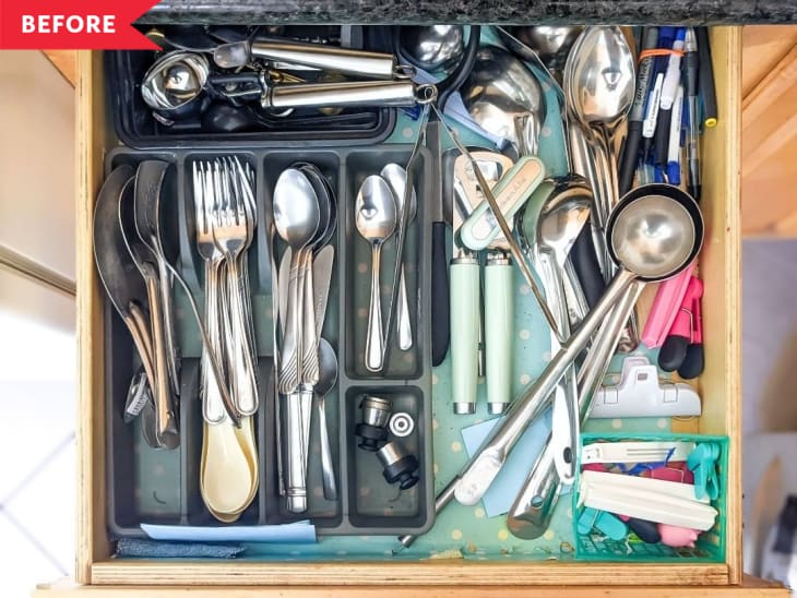 Cluttered kitchen drawer with assorted cutlery, ice cream scoops, pens, and clips in various compartments.