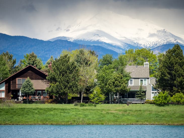 Homes with a lake in the foreground and a snowy mountain peak in the background.