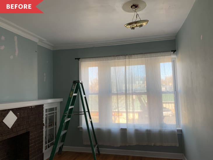 Living room with a brick fireplace, green ladder, sheer curtains, and an exposed ceiling light fixture.