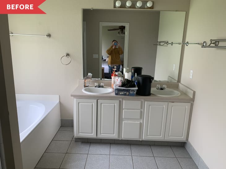 Bathroom with double sink vanity, cluttered countertop, large mirror, and bathtub.