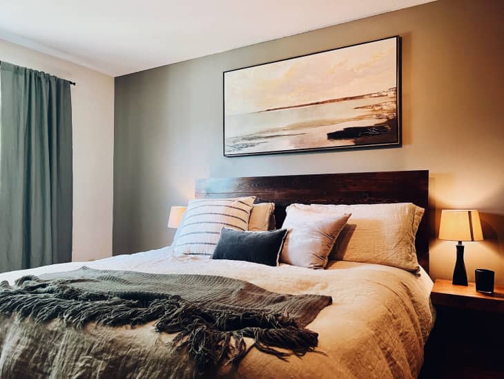 Cozy bedroom with a dark wood headboard, neutral bedding, abstract wall art, and bedside lamps.