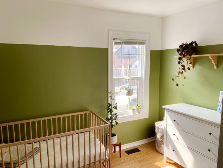 Sunny baby nursery with painted olive green walls on lower portion of the room with the top 1/3 painted white.