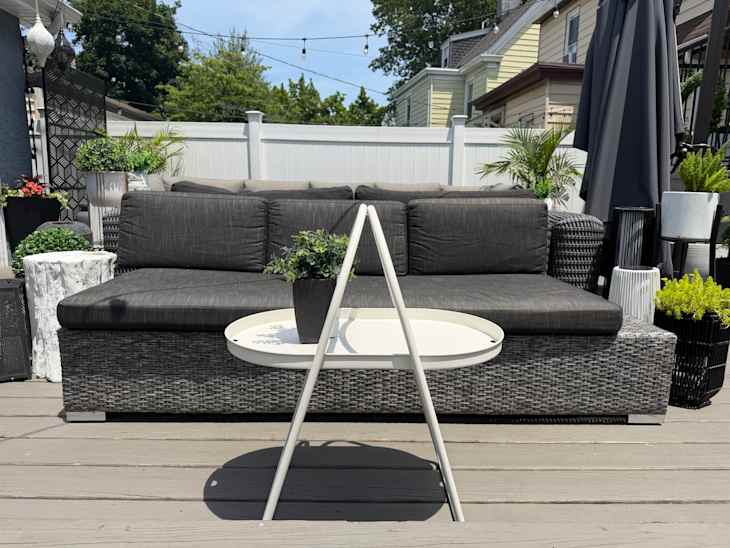 Outdoor seating area featuring a dark gray sectional sofa, a white round table, and various potted plants.