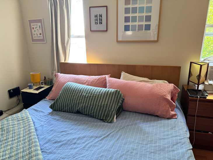 Cozy bedroom with a wooden bed, striped and solid color pillows, a bedside table with a lamp, and framed artwork on the wall.