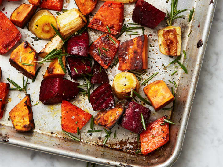 Roasted root vegetables with rosemary on a baking sheet.