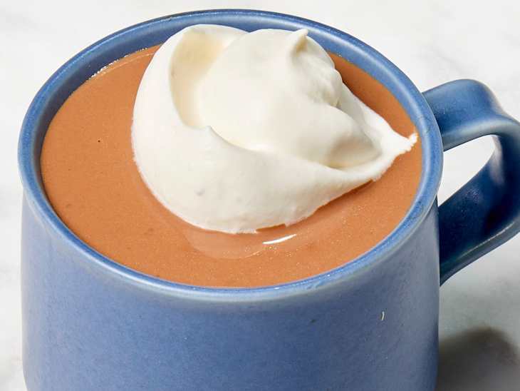 Angled shot of Jacques Torres' hot chocolate recipe in a dark blue mug, topped with whipped cream.