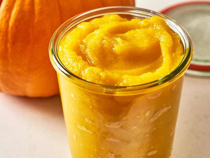 Image 3: A jar of bright orange pumpkin puree with a whole pumpkin in the background.