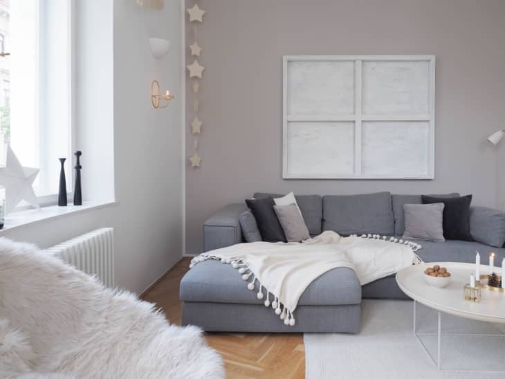 Gray sectional sofa with white throw blanket, round coffee table with candles, and star wall decor in a cozy living room.