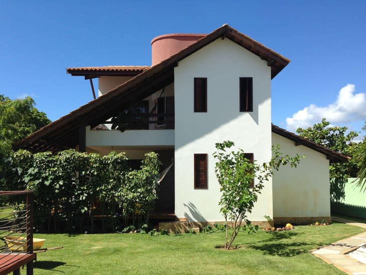 Two-story house with sloped roof, surrounded by lush greenery and a clear blue sky.