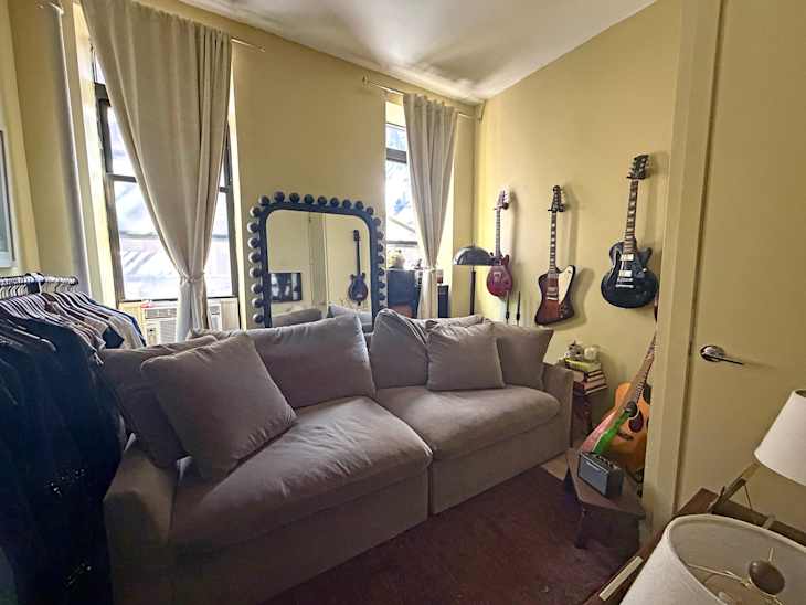 Cozy living space featuring a light-colored sofa, a large mirror, and several guitars on the wall.