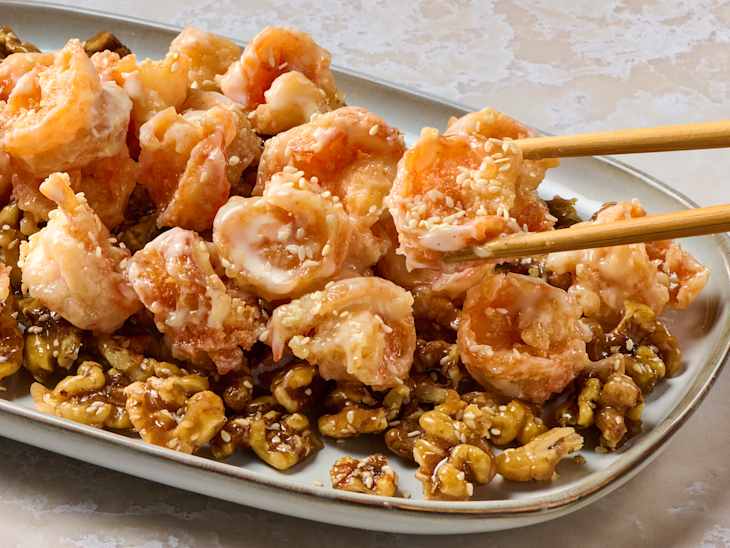 Crispy shrimp coated in a creamy sauce, garnished with sesame seeds, served with caramelized walnuts.