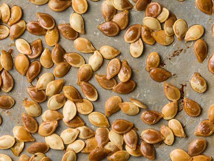 Image 2: Roasted pumpkin seeds scattered on a metal baking sheet, showcasing a mix of golden and brown hues.